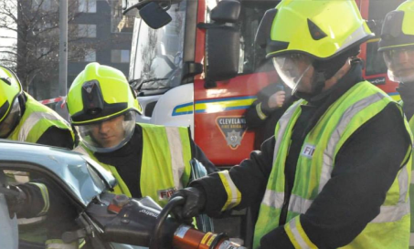 A group of firefighters using a heavy grinder to access a crashed car